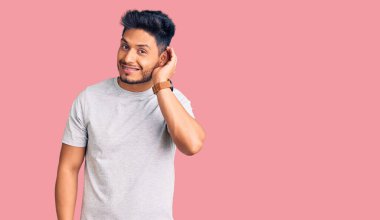 Yakışıklı Latin Amerikalı sıradan tişörtler giyen, el pençe divan gülümseyen dedikoduları ve dedikoduları dinleyen genç adam. Sağırlık kavramı. 