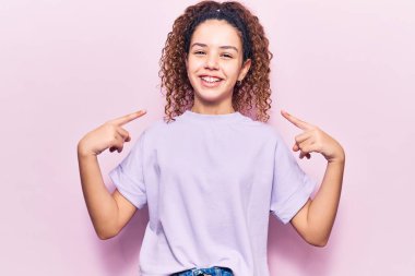 Beautiful kid girl with curly hair wearing casual clothes looking confident with smile on face, pointing oneself with fingers proud and happy.  clipart