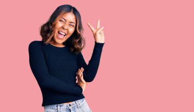 Genç, güzel, melez, sıradan kıyafetler giyen, gülen, kameraya göz kırpan, zafer işareti yapan bir kadın. İki numara.. 