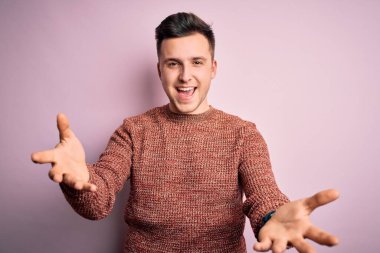 Pembe izole edilmiş arka plan üzerine sıradan bir kazak giyen yakışıklı beyaz adam gülümseyen, yardım eli uzatan ve kabullenen eller sunuyor..