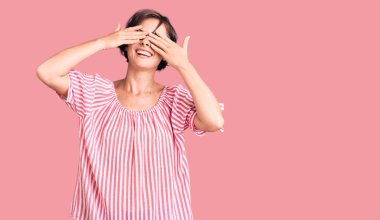 Kısa saçlı, günlük giysiler giyen, elleri gülücüklü, neşeli, gözleri kaplayan güzel bir genç kadın. kör kavram. 