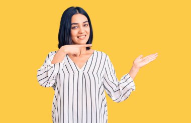 Gündelik giysiler giyen genç ve güzel Latin kadın kameraya hayret ediyor ve gülümsüyor.. 