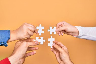 İzole edilmiş sarı arka planda bulmaca parçalarını birleştiren Kafkas gençlerinin elleri