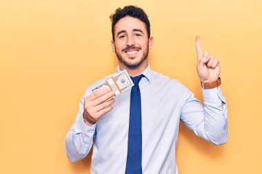 İş kıyafetleri giymiş genç İspanyol bir adam elinde dolarlarla bir fikir ya da soruyla gülümsüyor ve mutlu bir yüzle işaret ediyor. 