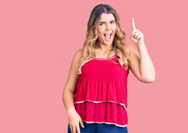 Gündelik giysiler giyen genç beyaz kadın başarılı bir fikirle işaret ediyor. Heyecanlı ve mutlu. Bir numara.. 