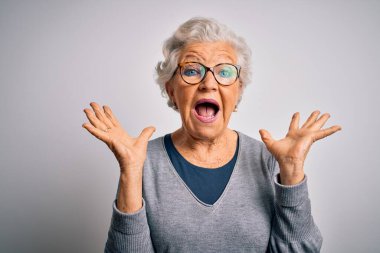 Senior beautiful grey-haired woman wearing casual sweater and glasses over white background celebrating crazy and amazed for success with arms raised and open eyes screaming excited. Winner concept clipart