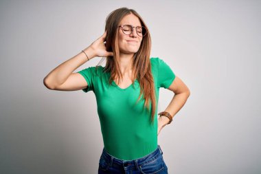 Genç, güzel, kızıl saçlı, sıradan yeşil tişört ve gözlük takan beyaz arka planda boynu ağrıyan, eliyle boynuna dokunan, kas ağrısı çeken bir kadın.
