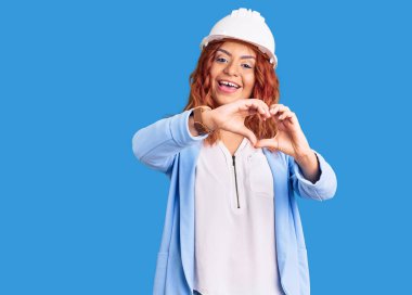 Mimar şapkası takan, aşık gülümseyen genç Latin kadın elleriyle kalp sembolü yapıyor. romantik kavram. 