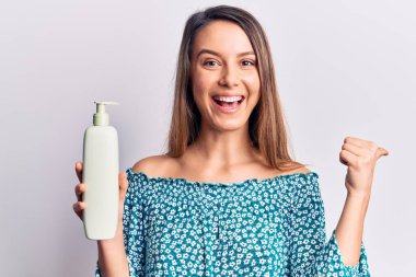 Genç, güzel bir kız, elinde krem losyon şişesiyle baş parmağını kaldırmış, ağzı açık gülümsüyor. 
