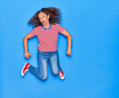 Orta yaşlı, güzel, İspanyol bir kadın. Günlük kıyafetler giyip mutlu gülümsüyor. İzole edilmiş mavi arka planda yüzünde gülümsemeyle zıplıyor