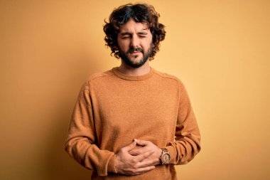 Sakallı genç yakışıklı bir adam sarı arka planda ayakta dikiliyor hazımsızlık, acı verici hastalıklar yüzünden. Ache kavramı.