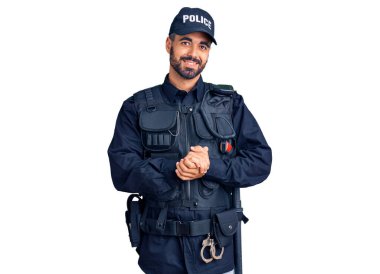 Polis üniforması giyen genç İspanyol adam ellerini kavuşturup gülümseyerek gevşemiş ve neşeli gülümsüyor. Başarı ve iyimserlik 