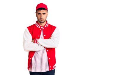 Beyzbol üniforması giyen genç İspanyol adam şüpheci ve gergin, yüzünde çapraz kollu tasvip etmeyen ifade. negatif kişi. 