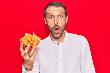 Elinde patates cipsi tutan genç yakışıklı adam ağzı açık kalmış, korkmuş ve şaşırmış. 