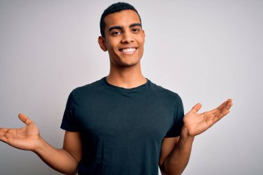 Beyaz arka plan üzerinde duran rahat tişört giyen genç ve yakışıklı Afro-Amerikan adam gülümseyerek avuçlarını açıyor, sunuyor ve reklam karşılaştırması yapıyor ve dengeyi sağlıyor.