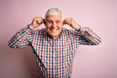 Üst düzey yakışıklı beyaz adam, pembe arka planda günlük bir gömlek giyiyor. Parmaklarıyla kulaklarını çekerek gülümsüyor. Komik bir jest. Seçme sorunu