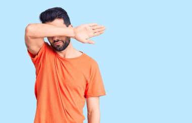 Sakallı, sıradan tişörtler giyen, gözlerini kollarıyla kapatan, ciddi ve üzgün görünen genç yakışıklı bir adam. Görme, saklama ve reddetme konsepti 