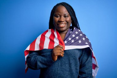 Genç, vatansever, Afro-Amerikan, örgü örgülü, mutlu yüzlü, kendine güvenen, gülümseyen ve dişlerini gösteren Amerikan bayrağı takan bir kadın.