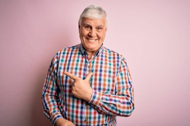 Son sınıftaki yakışıklı, beyaz gömlekli, soyutlanmış pembe arka planda neşeli, yüzünde bir gülümseme, mutlu ve doğal bir ifadeyle elini ve parmağını kaldırmış bir adam.