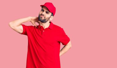 Sakallı, teslimat üniforması giyen boyun ağrısı çeken, eli boynuna dokunan, kas ağrısı çeken yakışıklı bir genç. 