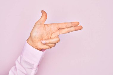 İzole edilmiş pembe arka planda parmaklarını gösteren beyaz bir gencin eli. Ateşli tabancayı parmaklarıyla işaret ediyor.