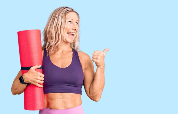 Middelbare Leeftijd Fit Blonde Vrouw Houden Yoga Mat Duim Wijzen — Stockfoto