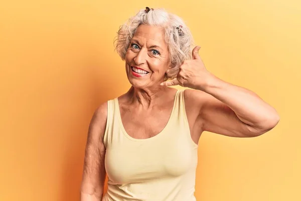 Senior grey-haired woman wearing casual clothes smiling doing phone gesture with hand and fingers like talking on the telephone. communicating concepts.