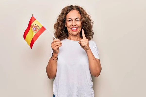 中年美丽的爱国女子举着西班牙国旗 高高地挂在孤独的白色背景上 微笑着 带着幸福的想法或问题指手画脚 位居第一 — 图库照片