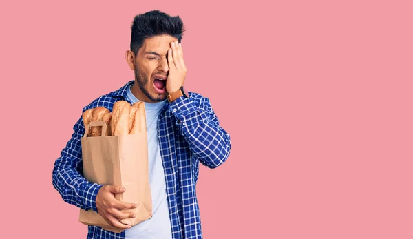 Guapo Joven Latinoamericano Sosteniendo Bolsa Papel Con Pan Bostezando Cansado —  Fotos de Stock