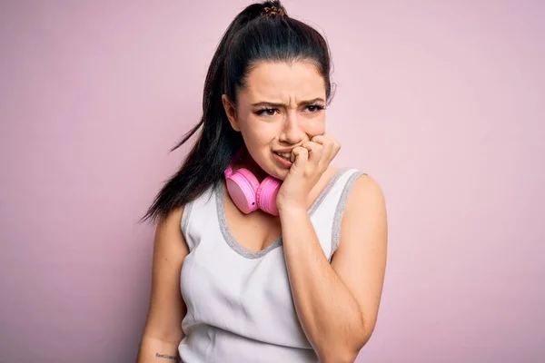 年轻的黑发女子 戴着健身房耳机 戴着粉色的隔离背景 看起来很紧张 双手放在咬指甲的嘴上 焦虑问题 — 图库照片