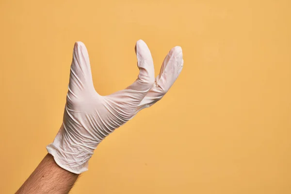 Ręka Białego Młodzieńca Rękawiczką Medyczną Nad Odizolowanym Żółtym Tłem Zbierającym — Zdjęcie stockowe