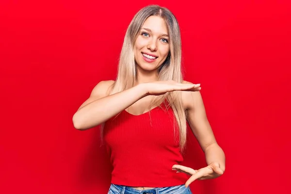 Young blonde woman wearing casual clothes gesturing with hands showing big and large size sign, measure symbol. smiling looking at the camera. measuring concept.