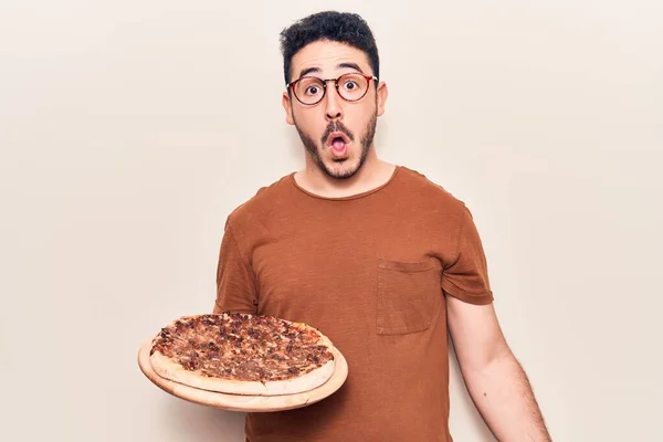 Young Hispanic Man Wearing Glasses Holding Italian Pizza Scared Amazed — Stock Photo, Image