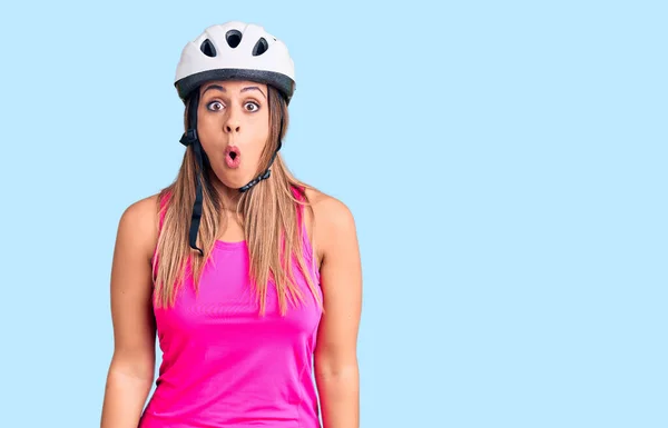 Young beautiful woman wearing bike helmet scared and amazed with open mouth for surprise, disbelief face