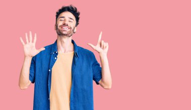 Gündelik kıyafetler giyen genç İspanyol adam yedi numarayı gösterip işaret ederken kendinden emin ve mutlu bir şekilde gülümsüyor.. 