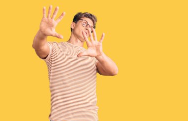 Sıradan kıyafetler ve gözlük takan genç yakışıklı adam korku ifadesinden korkuyor ve dehşete düşüyor. El hareketlerini bırak, şok içinde bağır. panik konsepti. 