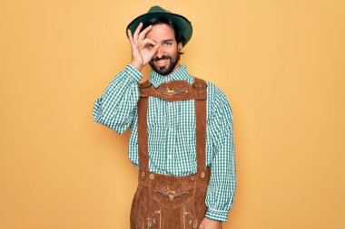 Almanya festivali için geleneksel Alman Ekim Festivali kıyafeti giyen genç yakışıklı adam el hareketleriyle gülümsüyor ve mutlu yüzüyle parmaklarının arasından bakıyor..