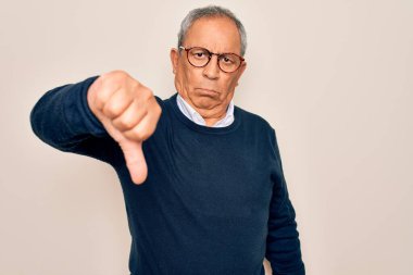 Üst düzey, gri saçlı, süveter ve gözlük takan, izole edilmiş beyaz arka planda mutsuz, kızgın, reddedilmiş ve olumsuz hareketler yapan bir adam. Kötü ifade.