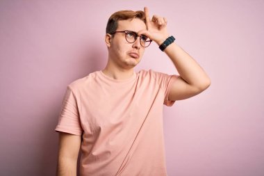 Genç, yakışıklı, günlük tişört giyen, pembe arka planda dikilen, alnında parmakları olan insanlarla alay eden ezik jestler yapan, alay eden, aşağılayan bir adam..