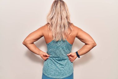 Orta yaşlı beyaz kadın spor giysisi giyiyor. Arkaya bakıyor. Kolları vücudunda. 