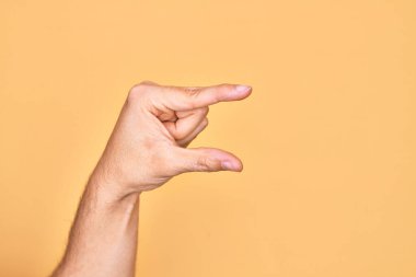 İzole edilmiş sarı arka plan üzerinde parmaklarını gösteren beyaz bir adamın eli. Görünmez bir şeyi alıp, parmaklarıyla uzayı gösteren bir nesneyi tutuyor.