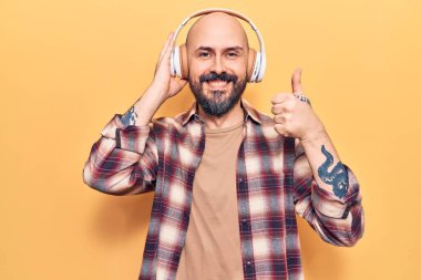 Müzik dinleyen, kulaklık takan, mutlu ve olumlu gülümseyen, başparmağını kaldıran, mükemmel ve onay işareti yapan genç yakışıklı bir adam. 