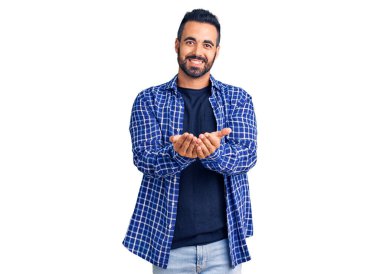 Elleri avuçlarında gülümseyen ya da el hareketi yapan gündelik kıyafetler giyen İspanyol genç bir adam. Bekleme ve koruma 