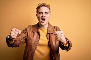 Genç, yakışıklı, deri ceket giyen, izole edilmiş sarı arka planda kızgın, kızgın ve öfkeliyken öfkeyle bağıran kızıl saçlı bir adam. Öfke ve agresif kavram.