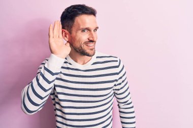 İzole edilmiş pembe arka planda dikilen sıradan çizgili süveter giyen genç ve yakışıklı bir adam. Kulağı kulağında, dedikoduları ve dedikoduları dinliyor. Sağırlık kavramı.