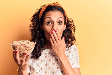 Orta yaşlı, güzel bir kadın elinde mısır gevreğiyle ağzı elle kaplanmış, şok olmuş ve hata yapmaktan korkan bir kâse tutuyor. şaşırmış ifade 