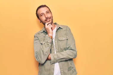 Gündelik giysiler giyen, kameraya kendinden emin, kolları çapraz ve çenesi havada gülümseyen genç yakışıklı bir adam. Olumlu düşünmek. 