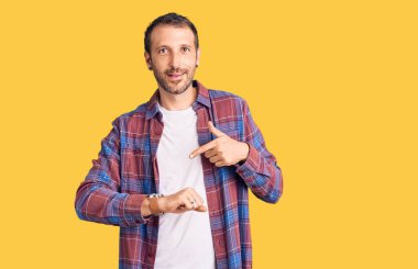 Gündelik giysiler giymiş genç yakışıklı adam, saati, sabırsızlığı, gecikme yüzünden kızgın ve sinirli olduğunu gösteriyor. 