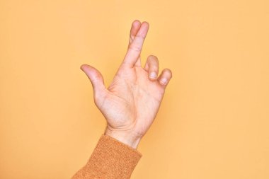 Kafkas genci parmaklarını izole edilmiş sarı arka plan üzerinde gösteriyor. Parmaklarını çapraz yapıyor, batıl inançlar ve şanslı bir jest, şanslı ve umut dolu bir ifade.