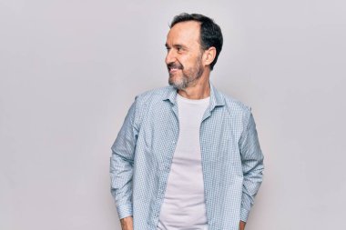 Orta yaşlı, sıradan bir kot gömlek giyen yakışıklı bir adam izole edilmiş beyaz arka planda duruyor, yan tarafa bakıyor, rahat bir görünüm takınıyor ve kendine güvenen bir gülümseme sergiliyor..